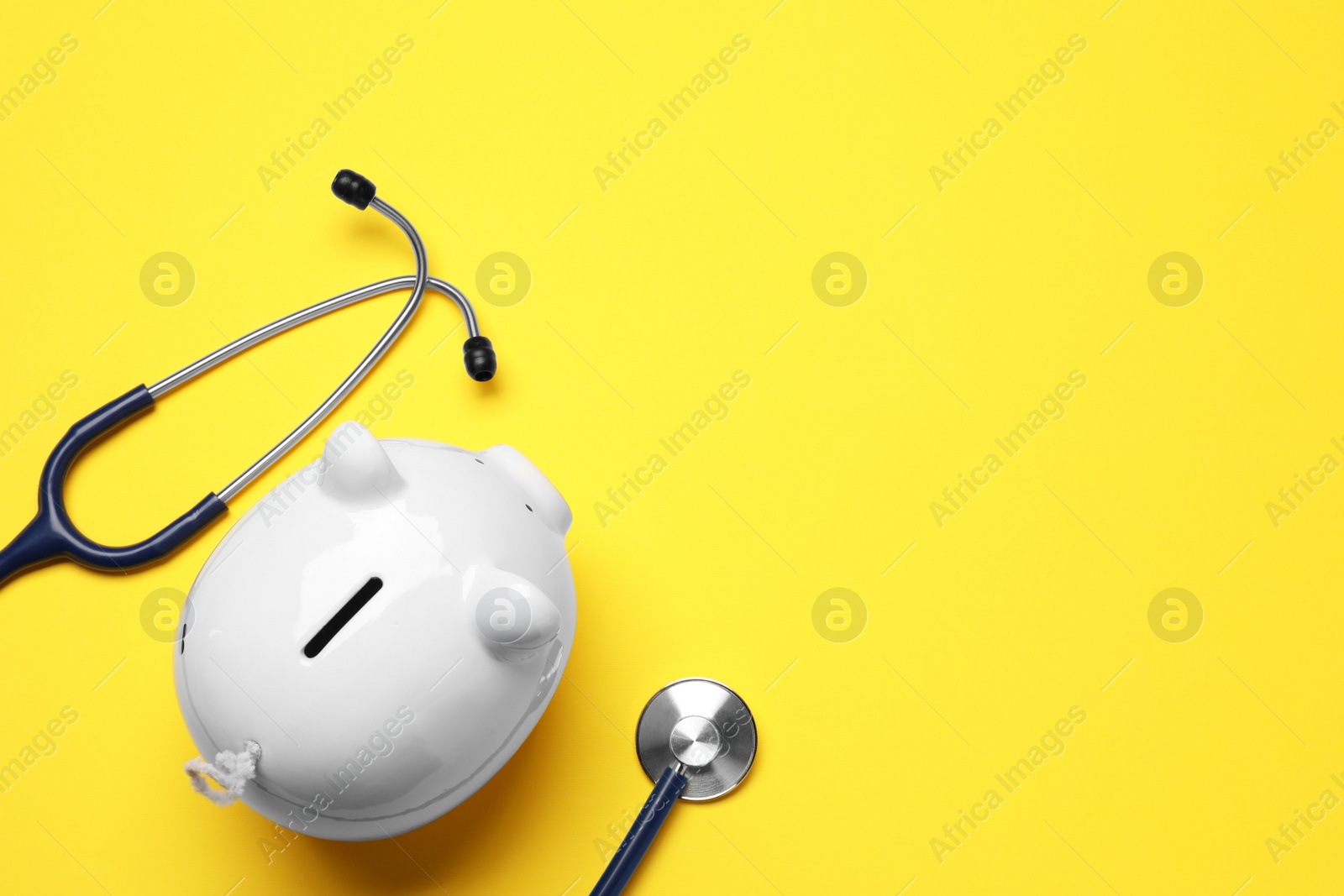 Photo of Piggy bank and stethoscope on yellow background, flat lay with space for text. Medical insurance