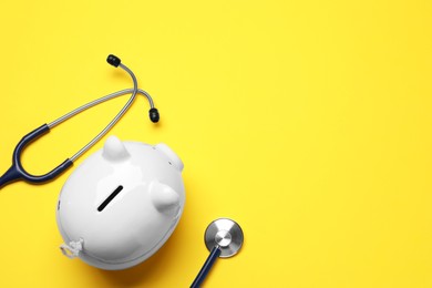 Photo of Piggy bank and stethoscope on yellow background, flat lay with space for text. Medical insurance