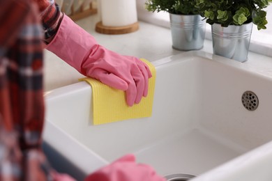 Photo of Woman cleaning kitchen sink with microfiber cloth at home, closeup