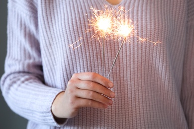 Photo of Woman in purple sweater holding burning sparklers, closeup