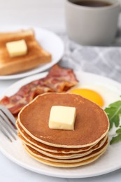 Tasty pancakes served with fried egg and bacon on white table