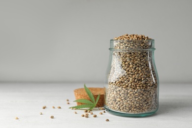 Photo of Organic hemp seeds in jar on white table. Space for text