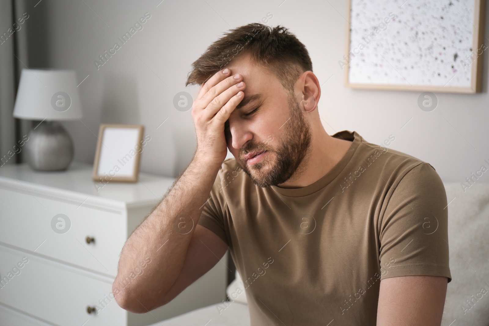 Photo of Young man suffering from migraine at home