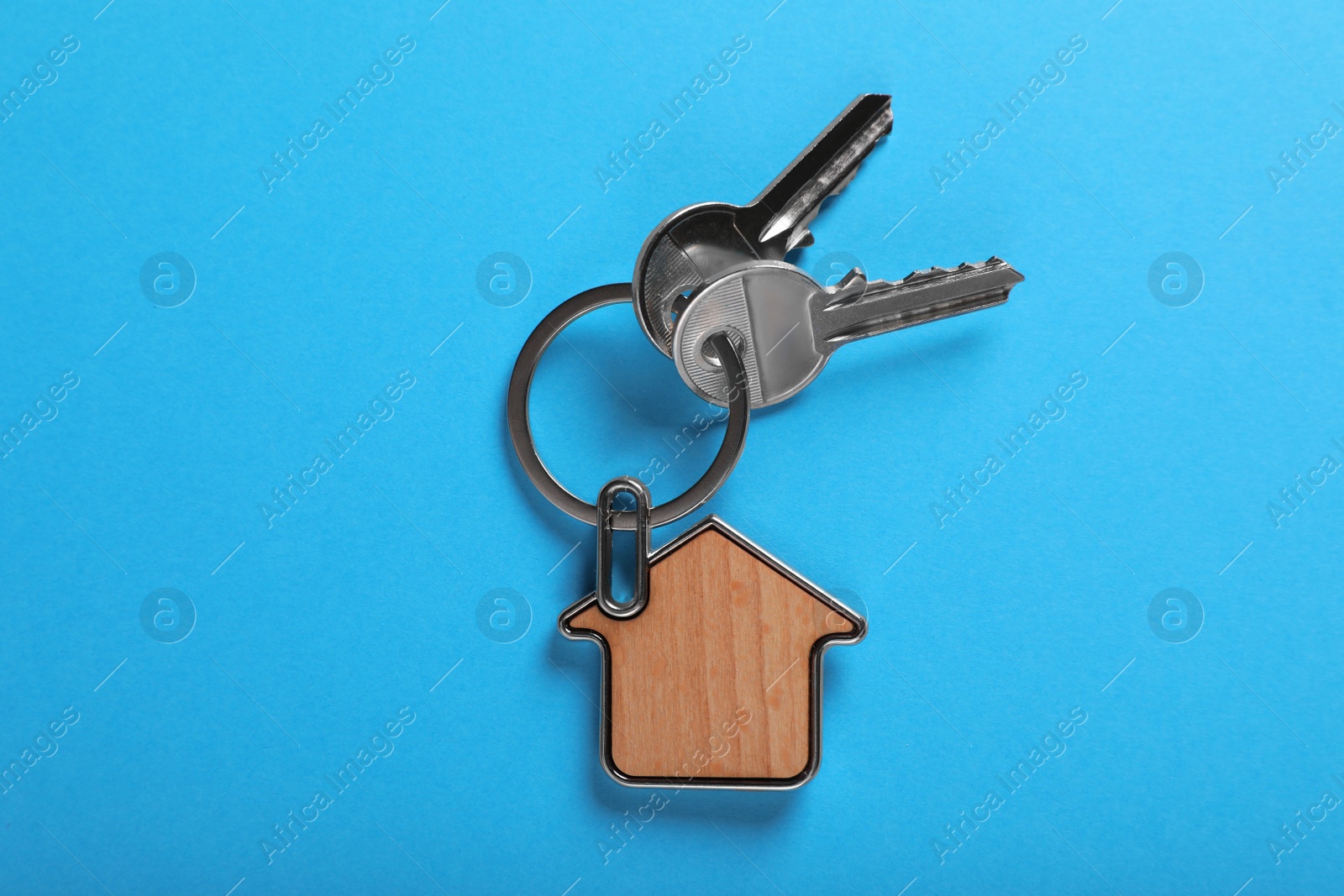 Photo of Keys with trinket in shape of house on blue background, top view. Real estate agent services