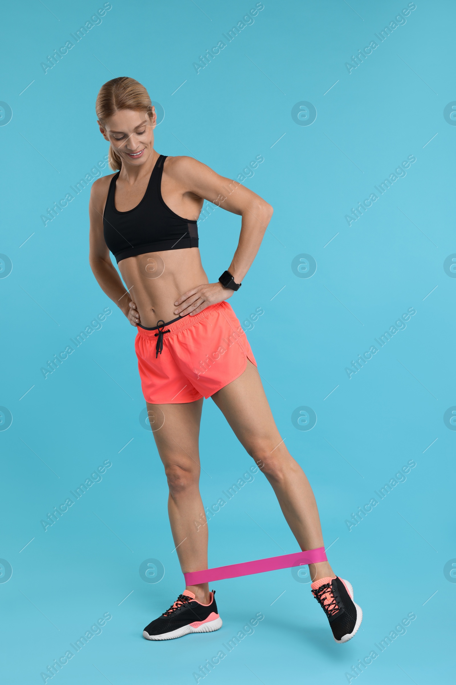 Photo of Woman exercising with elastic resistance band on light blue background