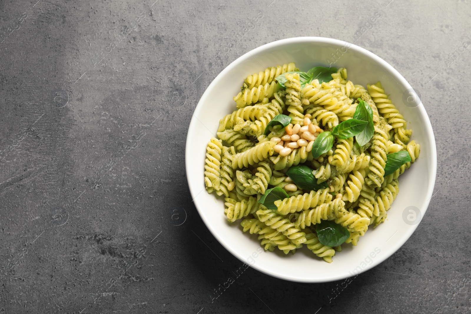 Photo of Plate of delicious basil pesto pasta and space for text on gray table, top view