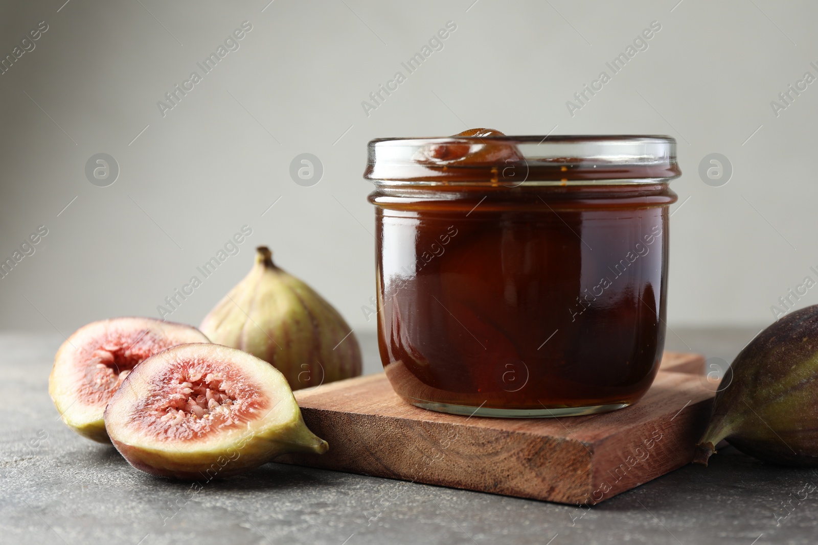 Photo of Jar of tasty sweet jam and fresh figs on grey table