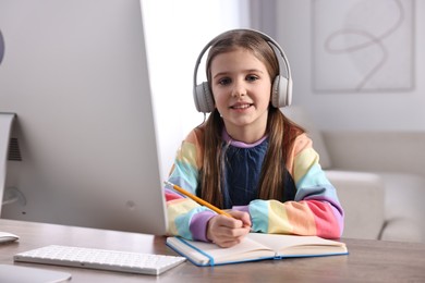 Photo of E-learning. Cute girl taking notes during online lesson at table indoors