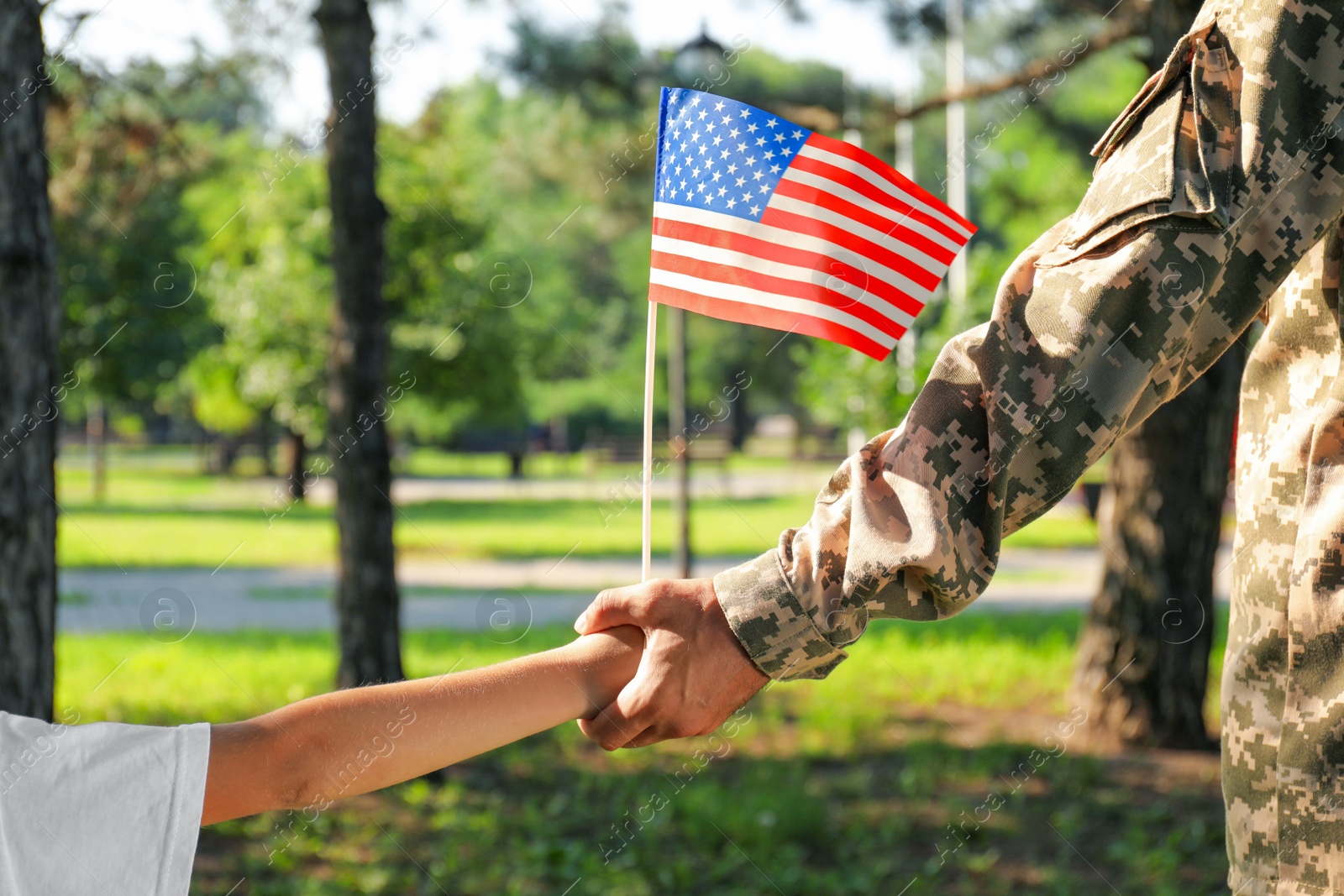 Photo of Soldier and his little son with American flag holding hands outdoors, closeup. Veterans Day in USA