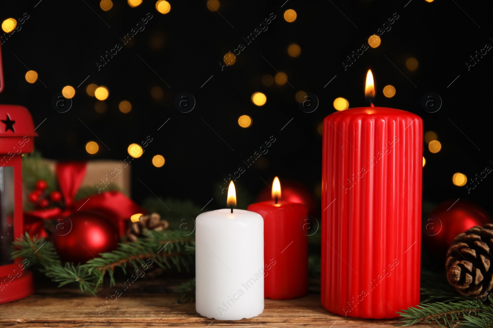 Photo of Burning candles and Christmas decor on wooden table against blurred festive lights