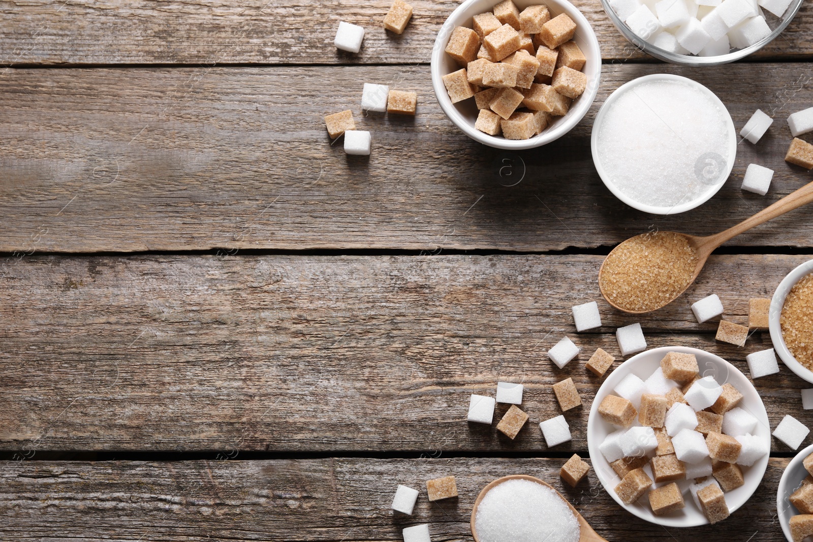 Photo of Different types of sugar in bowls and spoons on wooden table, flat lay. Space for text