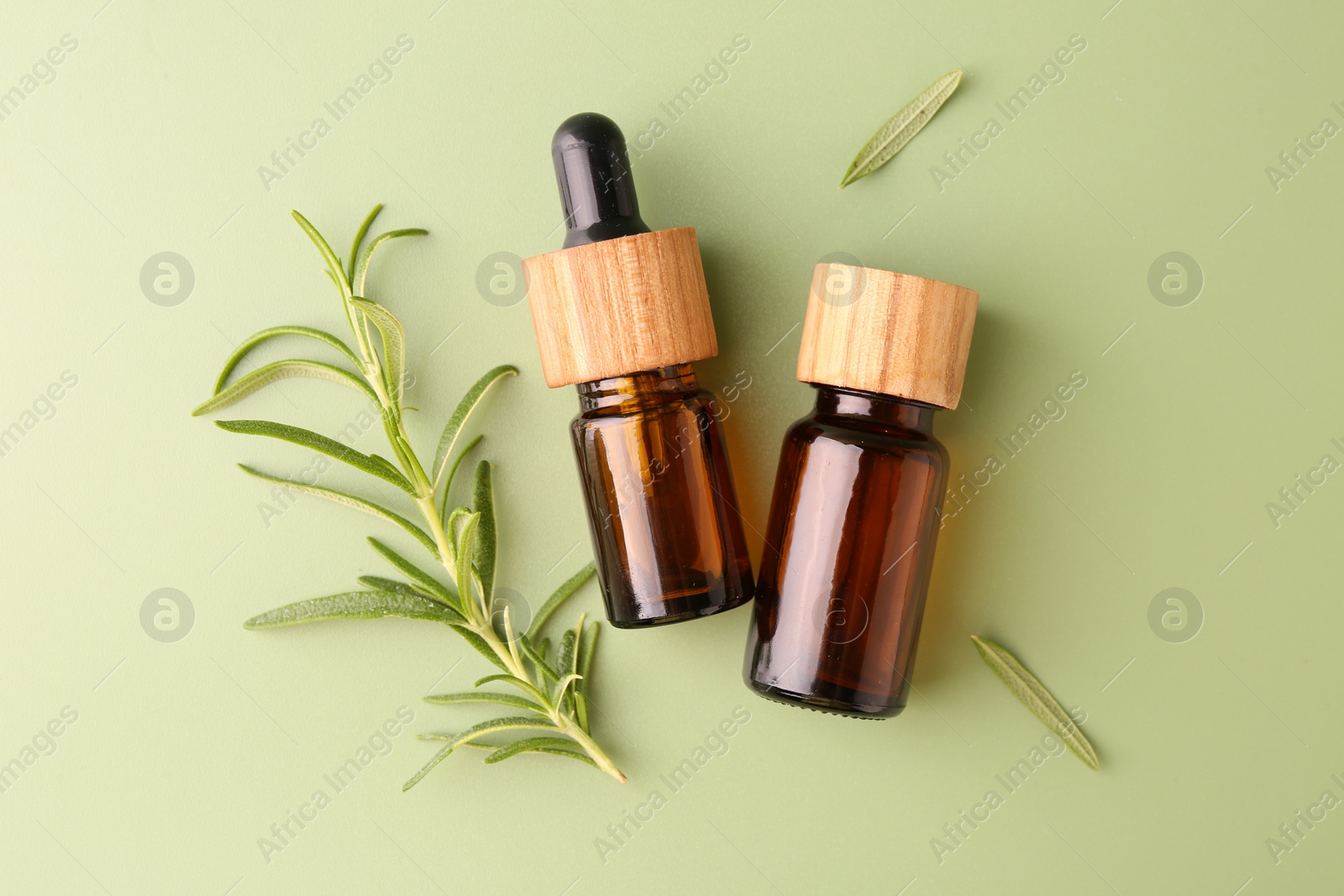 Photo of Aromatic essential oils in bottles and rosemary on green background, flat lay