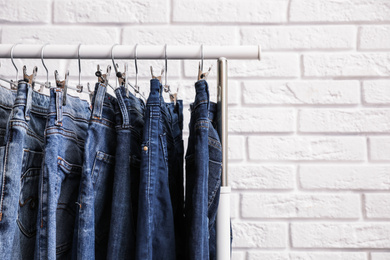 Rack with stylish jeans near brick wall, closeup