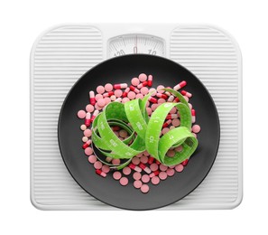 Scales with plate of pills and measuring tape on white background, top view