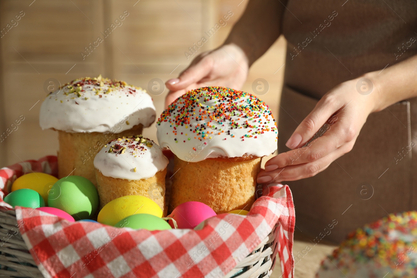 Photo of Woman putting traditional Easter cakes in basket indoors, closeup