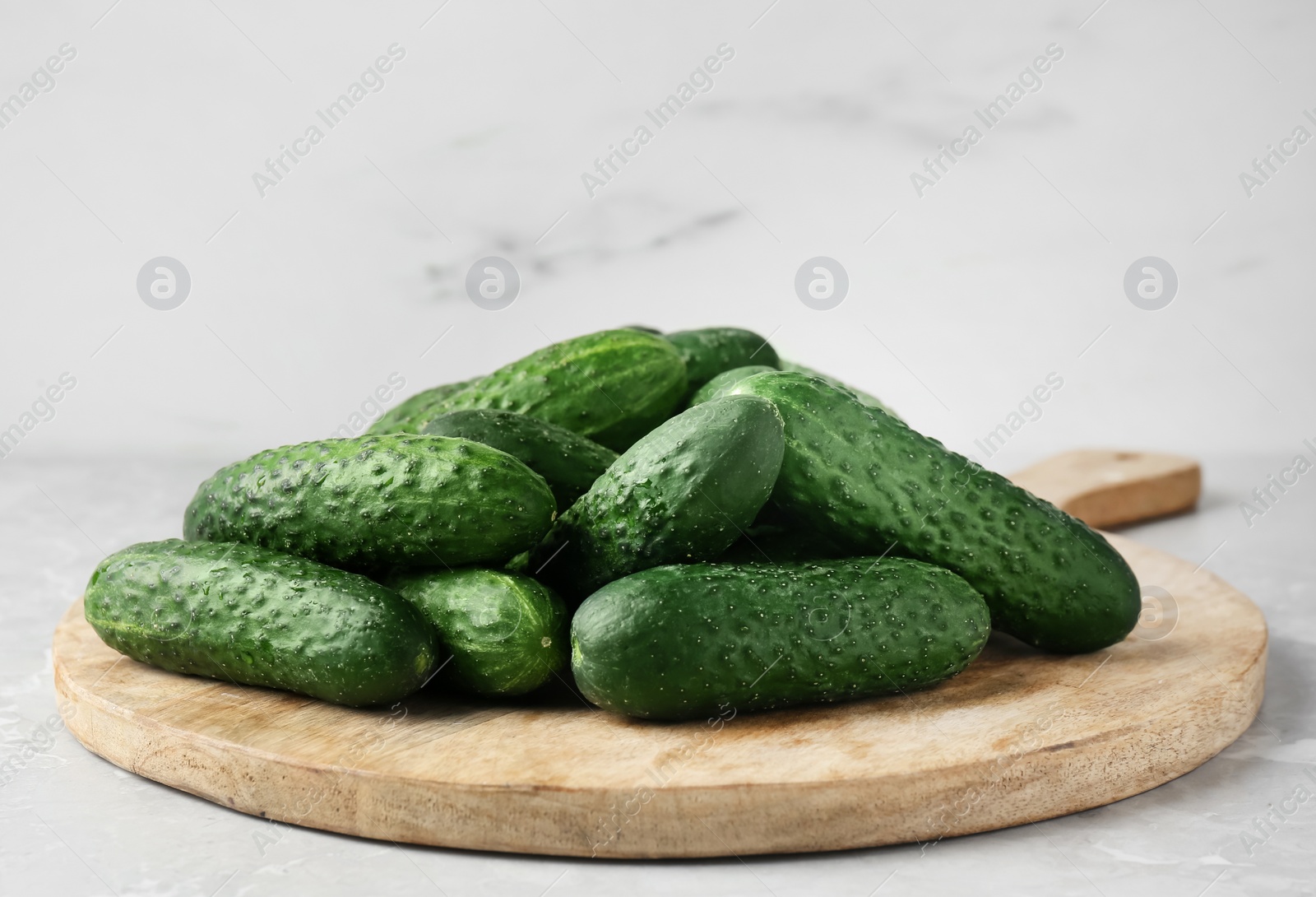 Photo of Board with fresh ripe cucumbers on white marble table