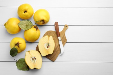 Photo of Tasty ripe quince fruits and knife on white wooden table, flat lay. Space for text