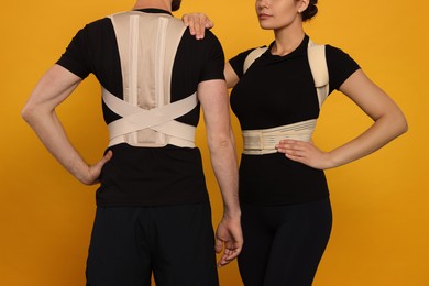 Closeup view of man and woman with orthopedic corsets on orange background