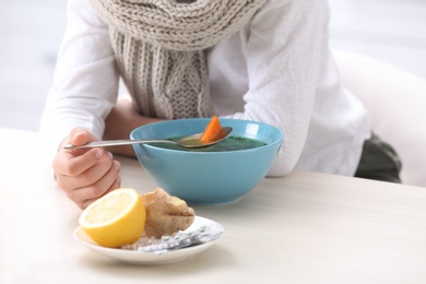 Photo of Sick little boy eating broth to cure cold at table in kitchen