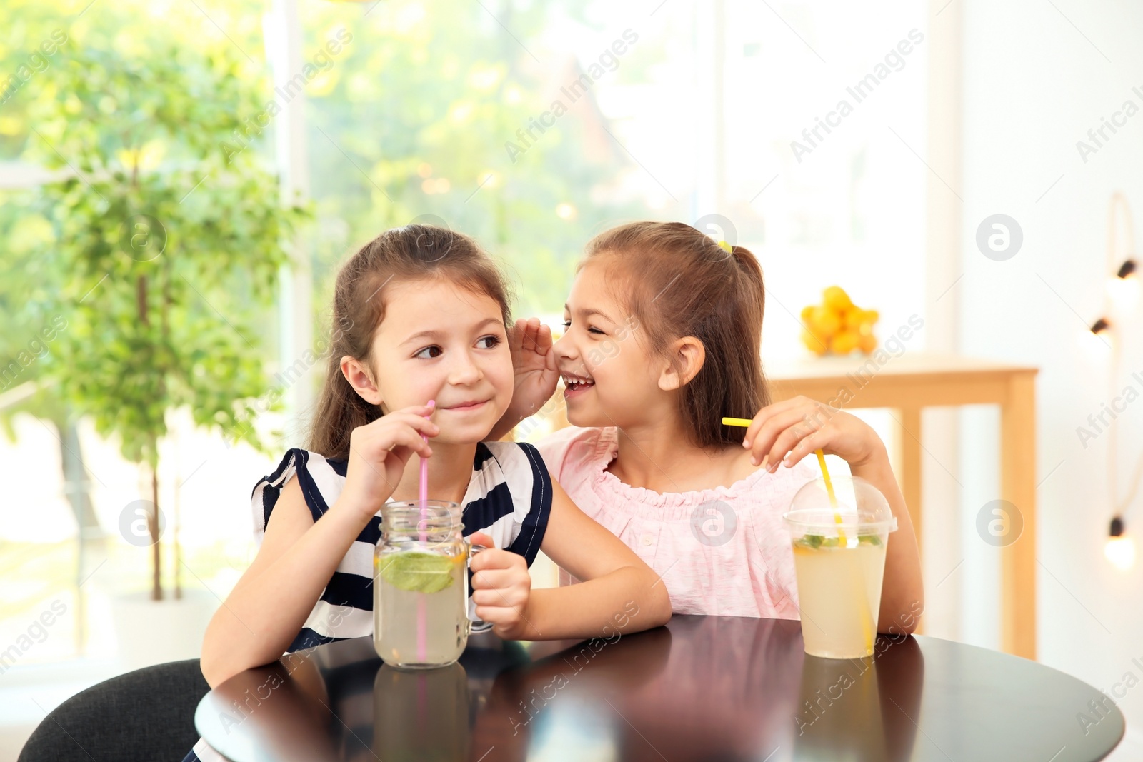 Photo of Little girls with natural lemonade at table indoors