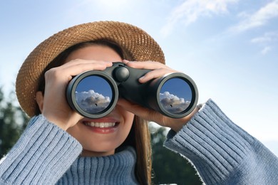 Image of Young woman with binoculars outdoors on sunny day. Sky with clouds reflecting in lenses