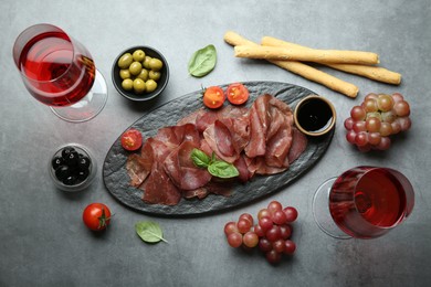 Delicious bresaola, wine and different products served on grey textured table, flat lay