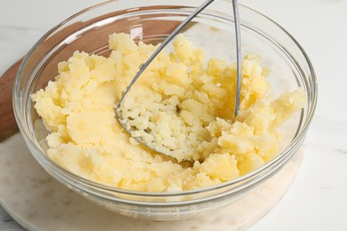 Bowl with delicious mashed potato and masher on white table, closeup