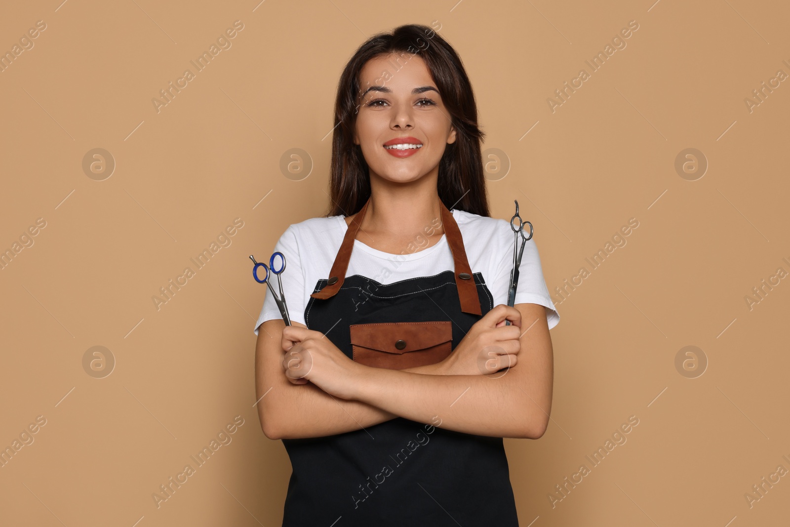 Photo of Portrait of happy hairdresser with professional scissors against pale orange background