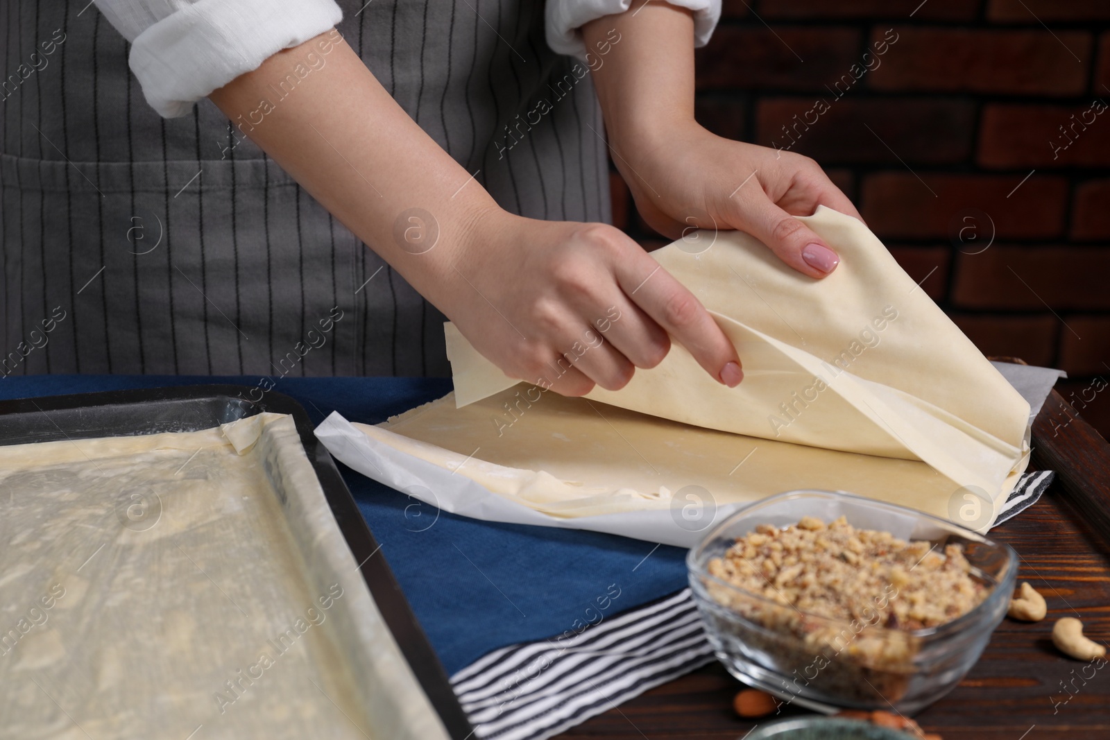 Photo of Making delicious baklava. Woman with dough at wooden table, closeup