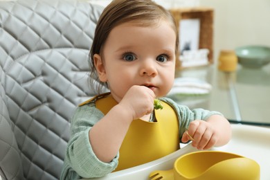 Cute little baby eating healthy food in high chair indoors