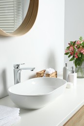 Photo of Vase with beautiful Alstroemeria flowers and toiletries near sink in bathroom