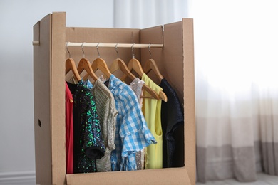 Photo of Cardboard wardrobe box with clothes on hangers indoors. Moving day