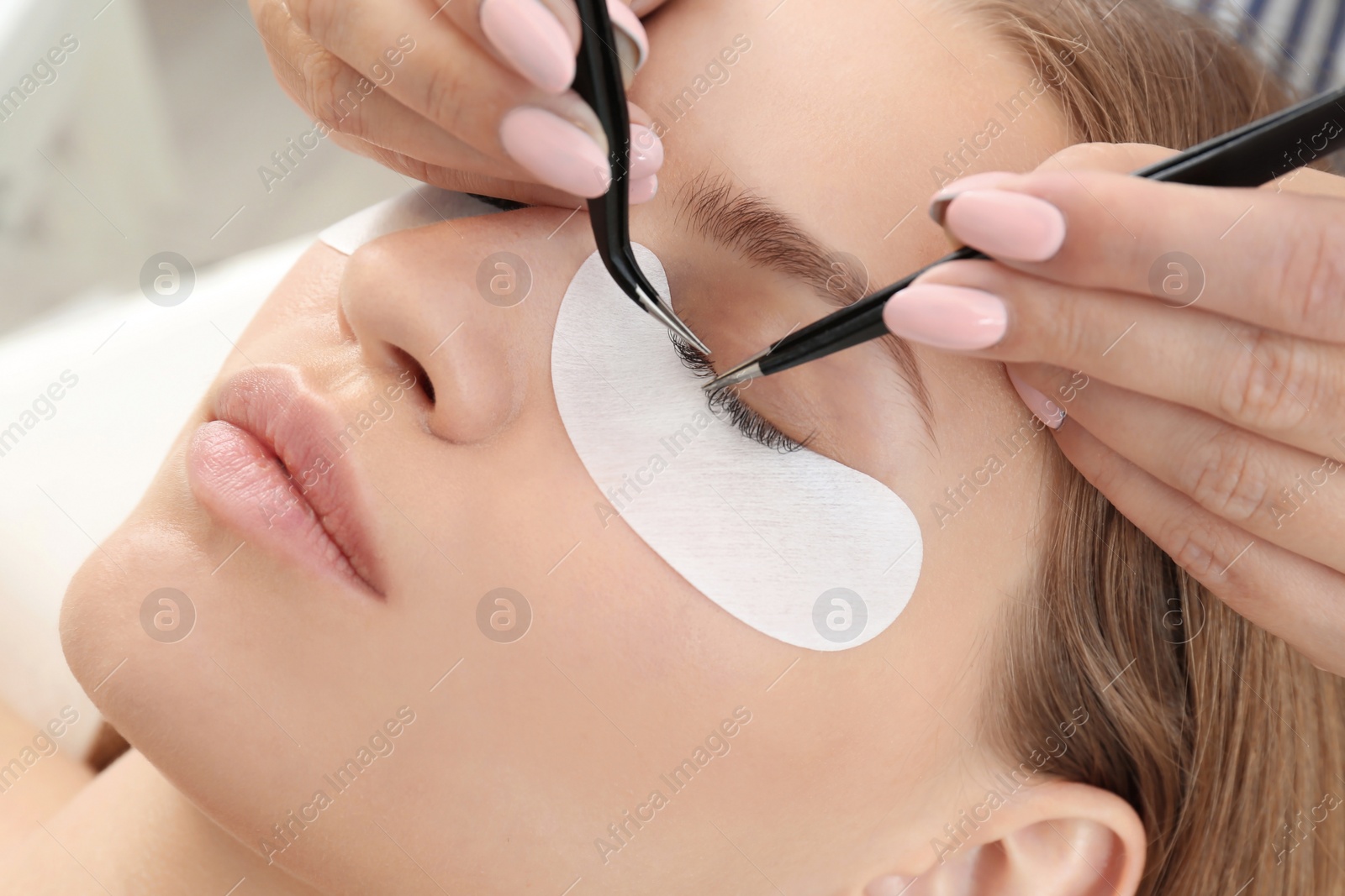 Photo of Young woman undergoing eyelash extensions procedure, closeup