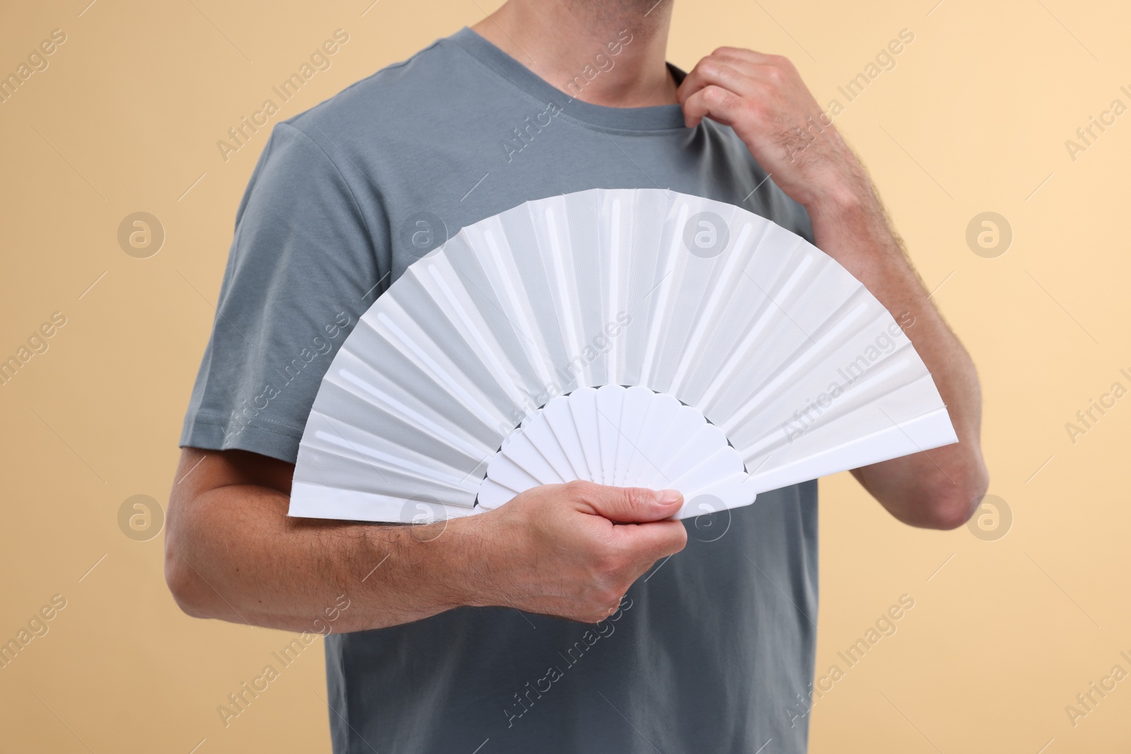 Photo of Man holding hand fan on beige background, closeup