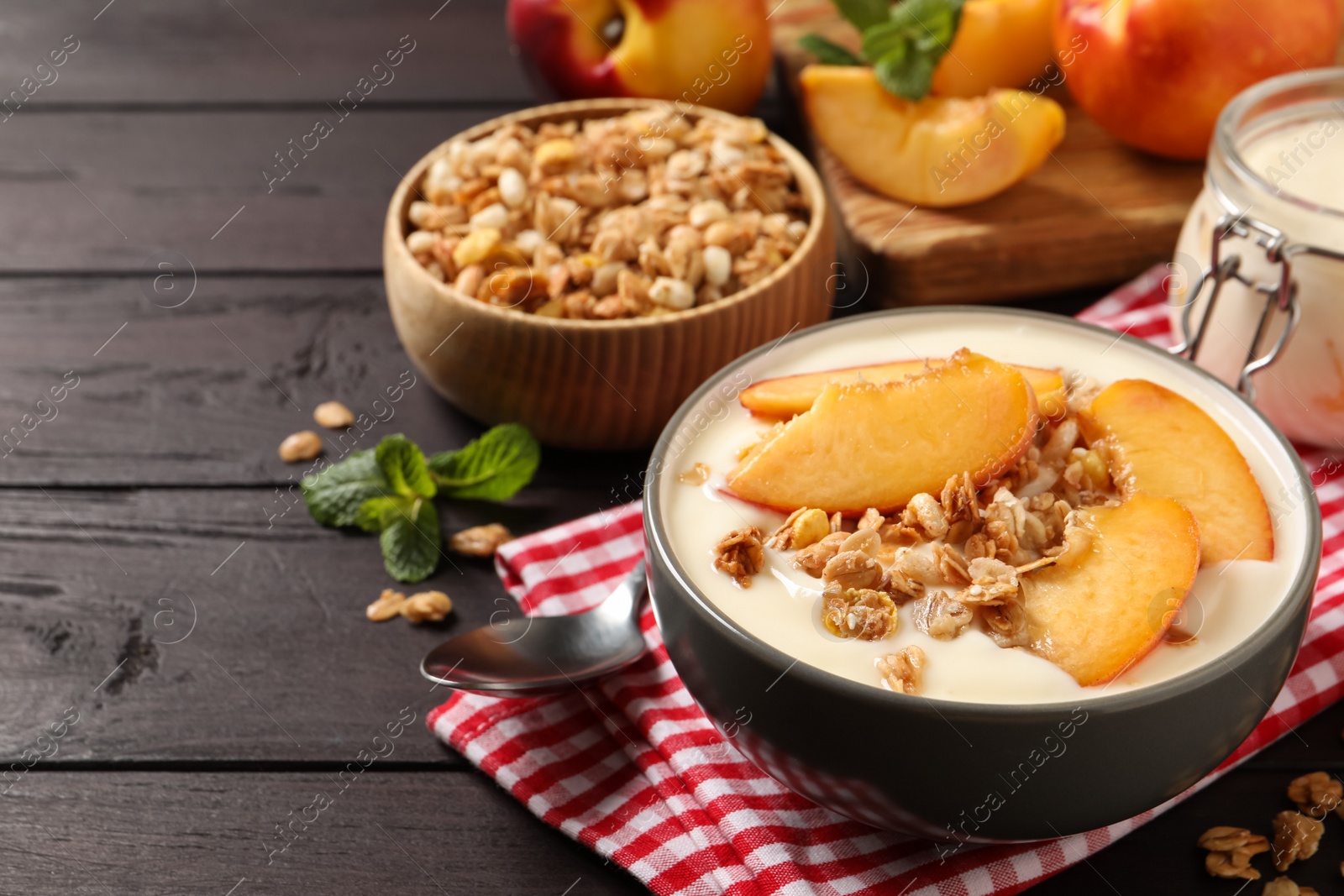 Photo of Tasty peach yogurt with granola and pieces of fruits in bowl on wooden table, space for text