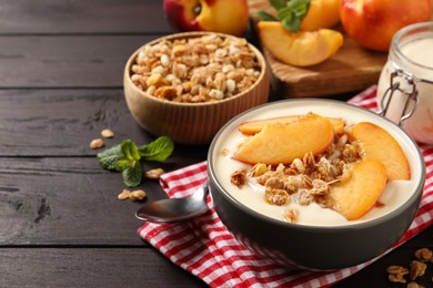 Photo of Tasty peach yogurt with granola and pieces of fruits in bowl on wooden table, space for text