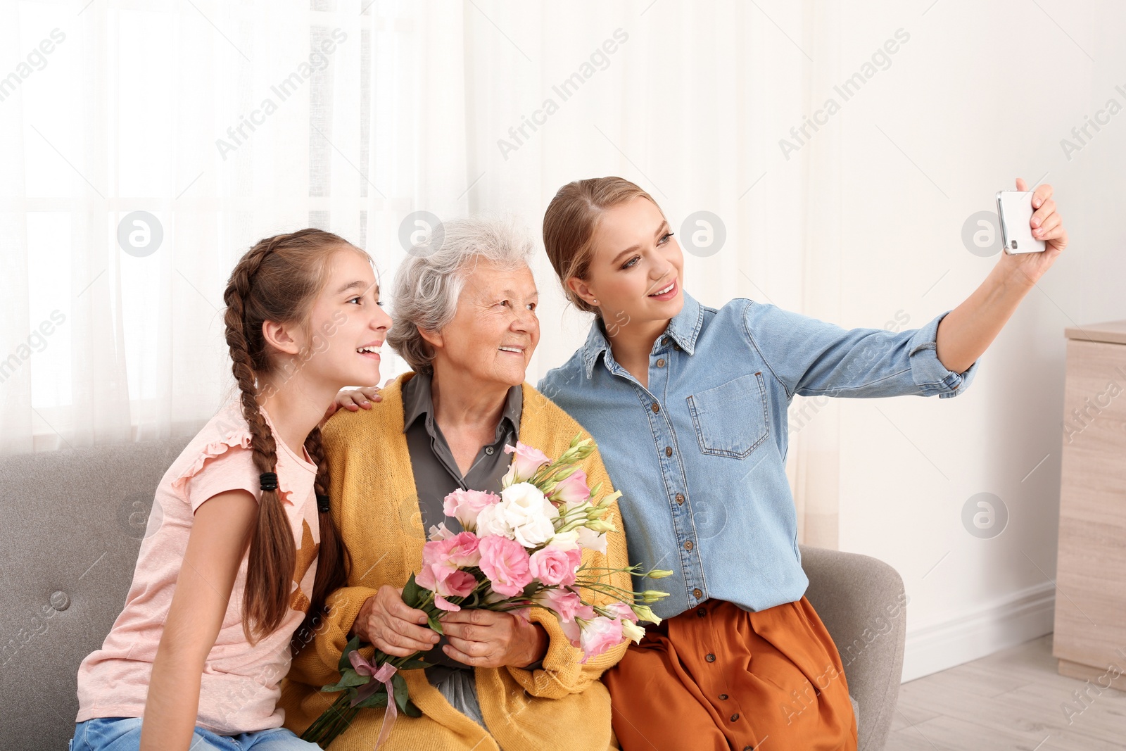 Photo of Happy sisters taking selfie with their grandmother holding flowers at home