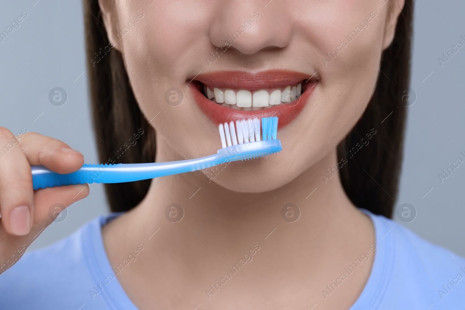 Photo of Woman brushing her teeth with plastic toothbrush on light grey background, closeup