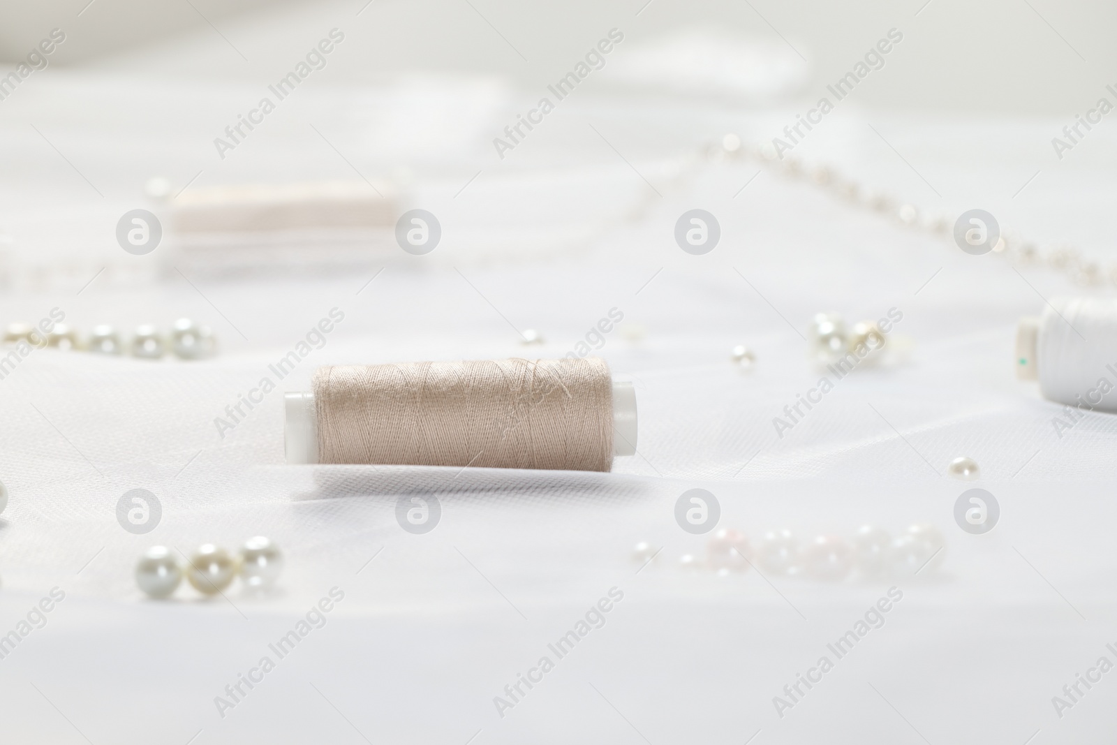 Photo of Spool of thread and beads on white fabric, closeup