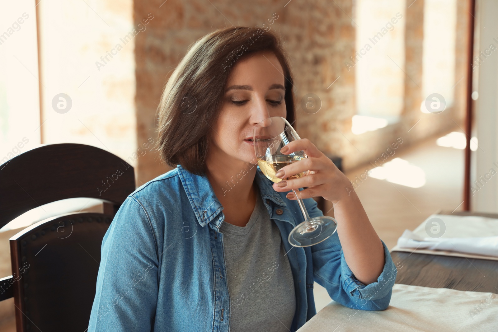 Photo of Woman with glass of white wine at table indoors