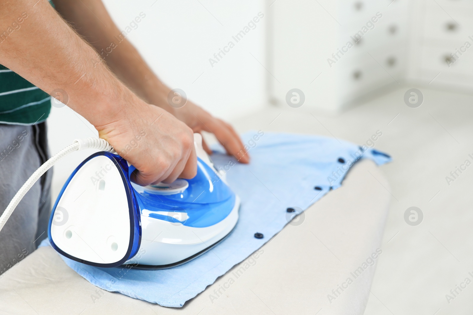 Photo of Man ironing shirt on board at home, closeup. Space for text