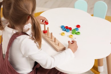 Photo of Little girl playing with stacking and counting game at white table indoors. Child's toy