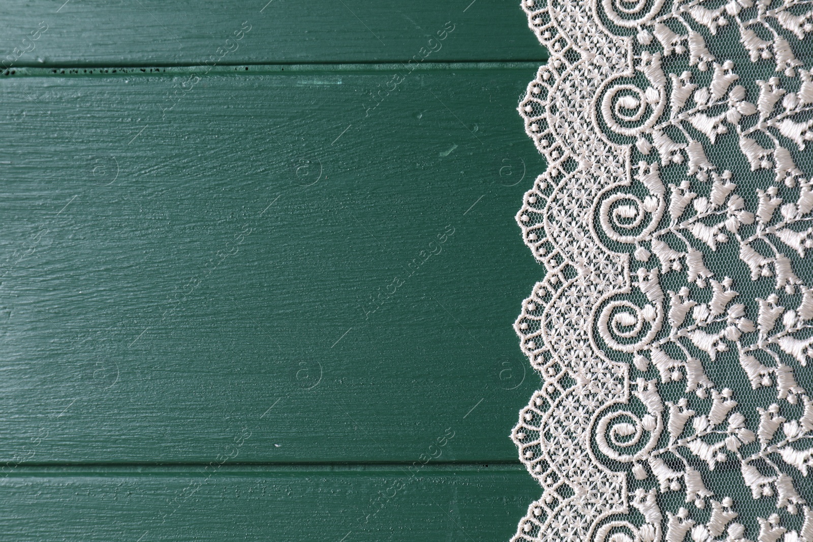 Photo of Beige lace on green wooden table, top view. Space for text