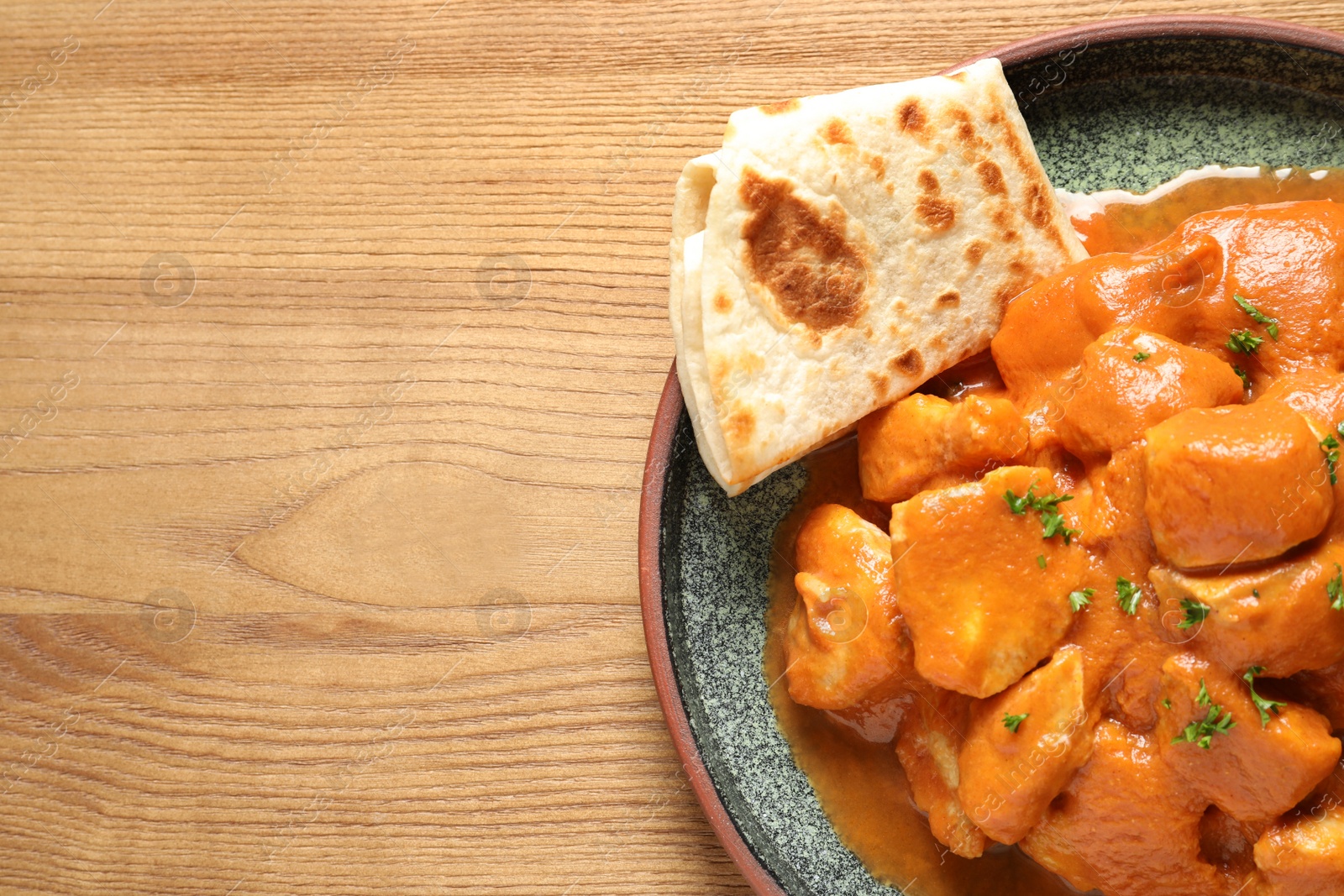 Photo of Delicious butter chicken on wooden table, top view with space for text. Traditional Murgh Makhani dish