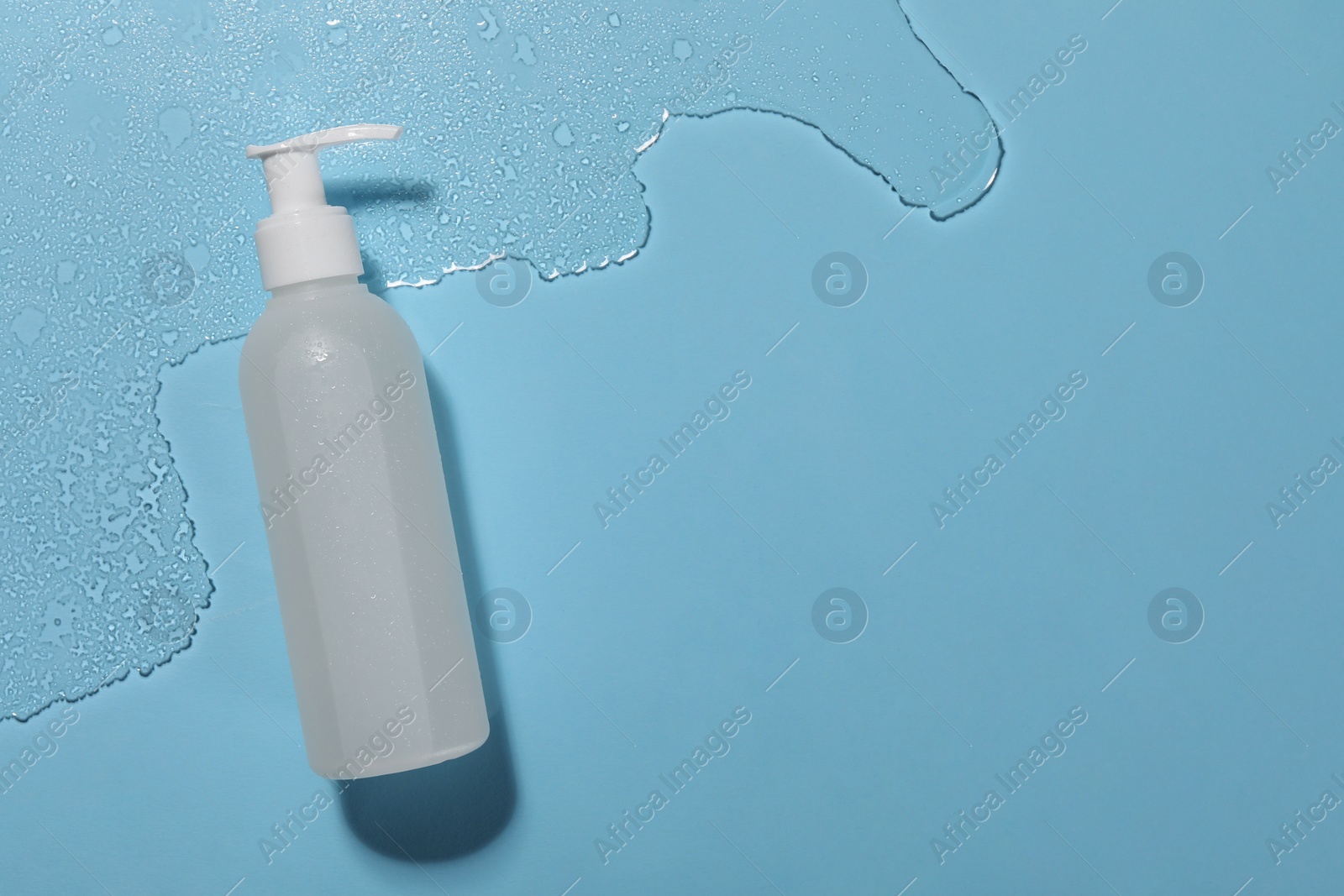 Photo of Bottle of face cleansing product in water against light blue background, top view. Space for text