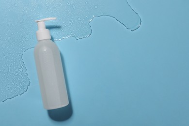 Bottle of face cleansing product in water against light blue background, top view. Space for text