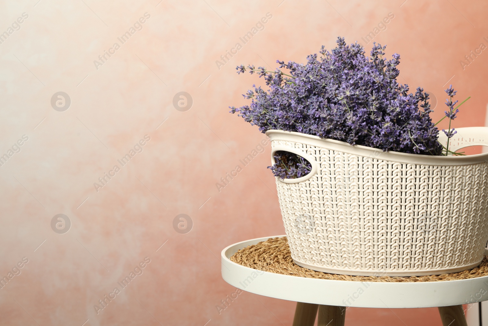 Photo of Beautiful lavender flowers in plastic basket on table against pink background. Space for text