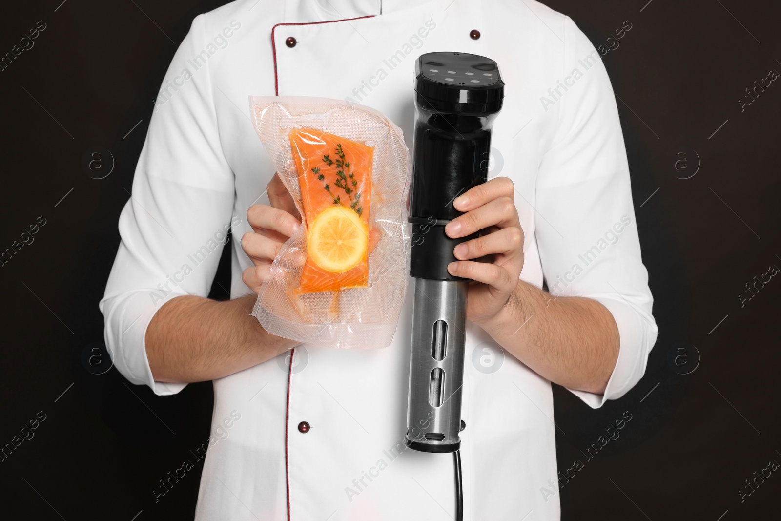 Photo of Chef holding sous vide cooker and salmon in vacuum pack on black background, closeup