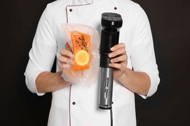 Chef holding sous vide cooker and salmon in vacuum pack on black background, closeup