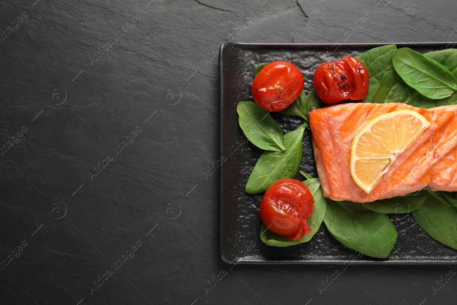Photo of Tasty grilled salmon with tomatoes, spinach and lemon on black table, top view. Space for text